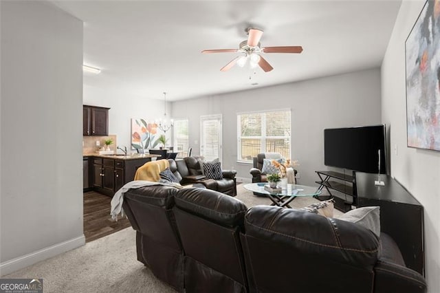 carpeted living room featuring ceiling fan with notable chandelier and sink