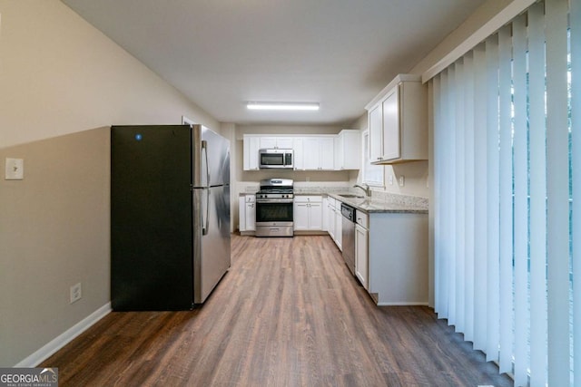 kitchen with appliances with stainless steel finishes, white cabinetry, sink, light stone countertops, and dark wood-type flooring