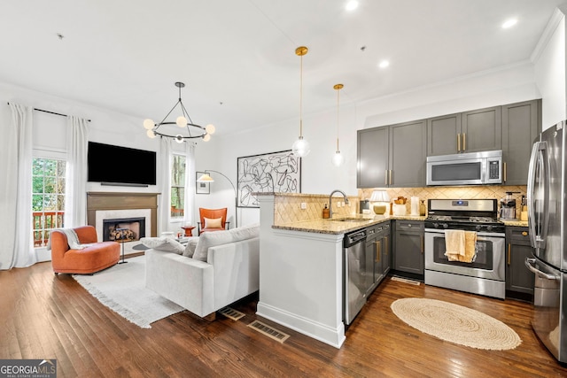 kitchen with sink, light stone counters, appliances with stainless steel finishes, kitchen peninsula, and pendant lighting