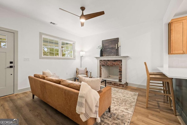 living room with ceiling fan, hardwood / wood-style floors, and a brick fireplace