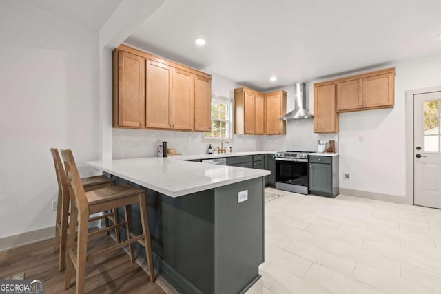 kitchen with tasteful backsplash, stainless steel electric range oven, wall chimney range hood, and a kitchen breakfast bar