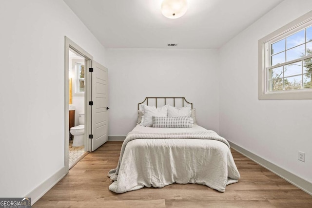 bedroom with ensuite bathroom and light hardwood / wood-style flooring