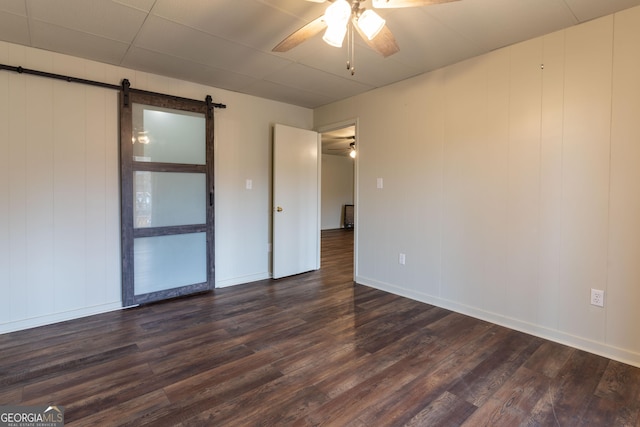 unfurnished room featuring dark hardwood / wood-style flooring, a barn door, and ceiling fan