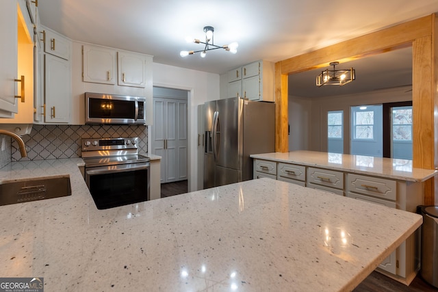 kitchen featuring appliances with stainless steel finishes, sink, a chandelier, hanging light fixtures, and light stone countertops