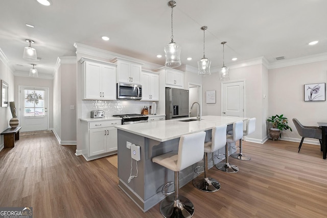 kitchen featuring white cabinetry, a kitchen island with sink, sink, appliances with stainless steel finishes, and a kitchen bar