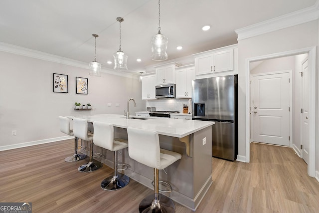 kitchen with a kitchen island with sink, sink, appliances with stainless steel finishes, white cabinets, and pendant lighting