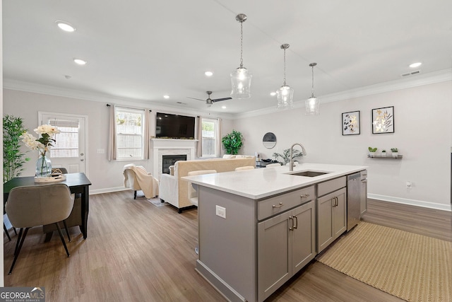 kitchen featuring a center island with sink, stainless steel dishwasher, gray cabinets, ornamental molding, and sink