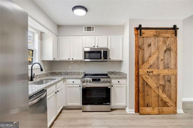 kitchen with sink, appliances with stainless steel finishes, a barn door, light stone countertops, and white cabinets