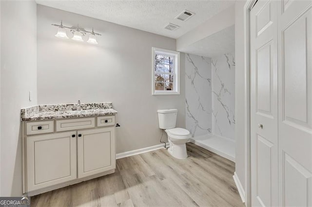 bathroom with hardwood / wood-style flooring, vanity, walk in shower, toilet, and a textured ceiling