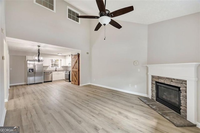 unfurnished living room with a fireplace, a barn door, ceiling fan, and light wood-type flooring