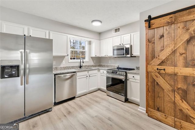 kitchen featuring sink, appliances with stainless steel finishes, white cabinetry, light stone countertops, and a barn door