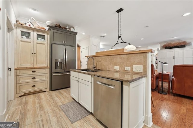 kitchen with sink, appliances with stainless steel finishes, light hardwood / wood-style floors, decorative light fixtures, and dark stone counters