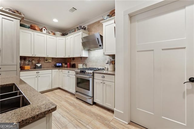 kitchen featuring wall chimney range hood, sink, dark stone countertops, gas stove, and white cabinets