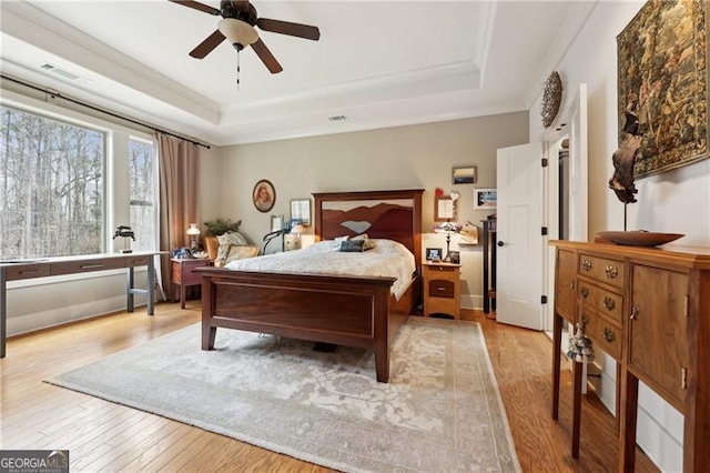 bedroom with ornamental molding, a raised ceiling, ceiling fan, and light wood-type flooring