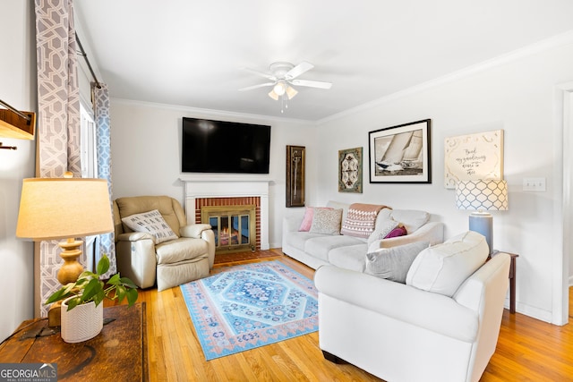 living room featuring wood-type flooring, a brick fireplace, ornamental molding, and ceiling fan