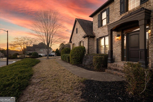 property exterior at dusk featuring brick siding and a shingled roof