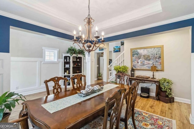 dining area featuring crown molding, an inviting chandelier, light wood-type flooring, and a tray ceiling