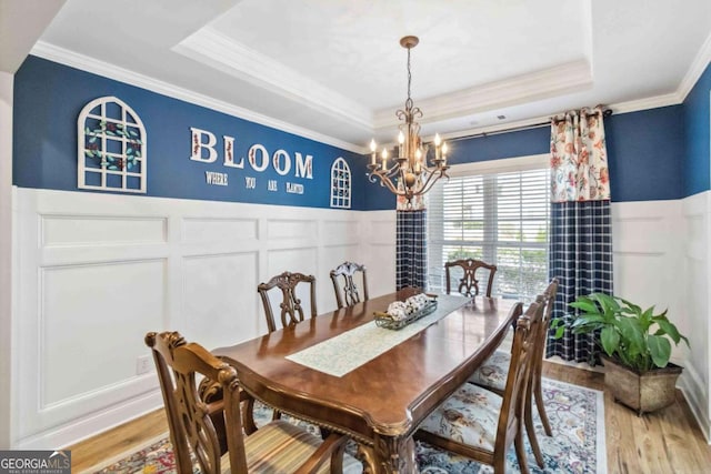 dining area with a chandelier, crown molding, a raised ceiling, and hardwood / wood-style floors