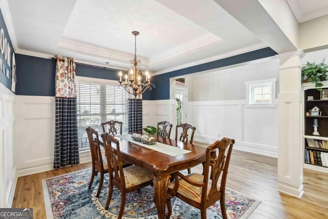 dining space featuring ornamental molding, a raised ceiling, a notable chandelier, hardwood / wood-style flooring, and decorative columns