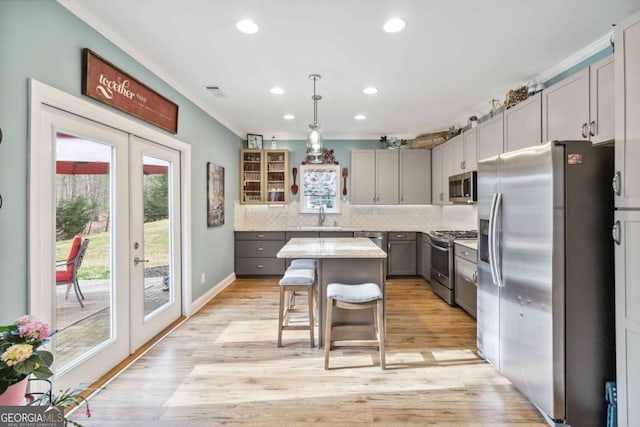 kitchen with gray cabinetry, decorative light fixtures, appliances with stainless steel finishes, a kitchen breakfast bar, and a kitchen island