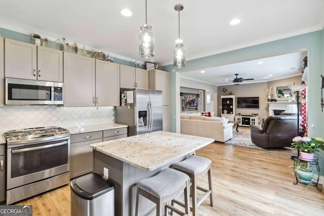 kitchen featuring gray cabinets, a breakfast bar, stainless steel appliances, light stone counters, and ornamental molding