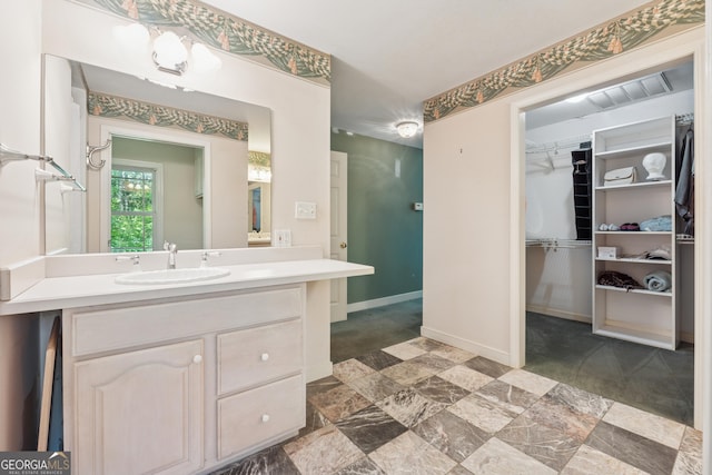 bathroom with a walk in closet, vanity, visible vents, and baseboards