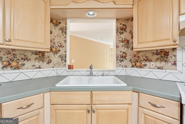kitchen with light brown cabinets, a sink, dark countertops, wainscoting, and wallpapered walls