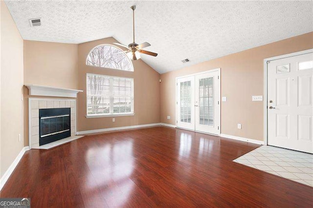 unfurnished living room with hardwood / wood-style flooring, lofted ceiling, a tiled fireplace, and french doors