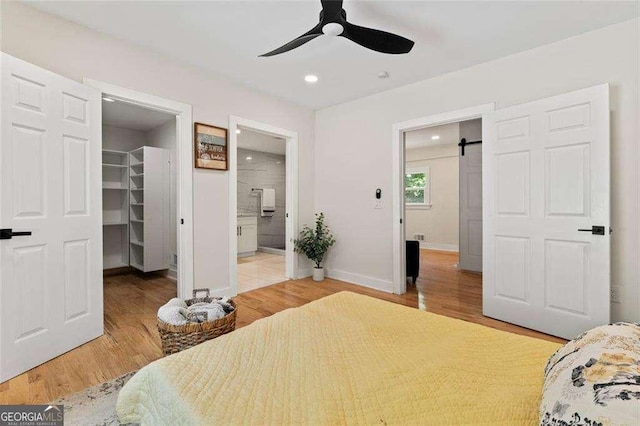 bedroom with ensuite bathroom, a walk in closet, wood-type flooring, a closet, and a barn door