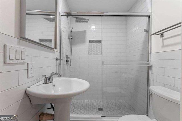 bathroom featuring toilet, a shower with shower door, and tile walls