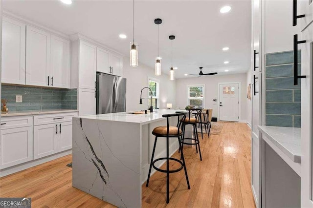 kitchen with stainless steel refrigerator, sink, an island with sink, and white cabinets