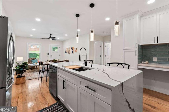 kitchen with sink, appliances with stainless steel finishes, light stone counters, an island with sink, and white cabinets