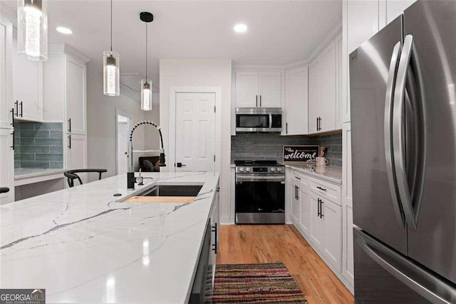 kitchen featuring sink, hanging light fixtures, stainless steel appliances, light stone counters, and white cabinets