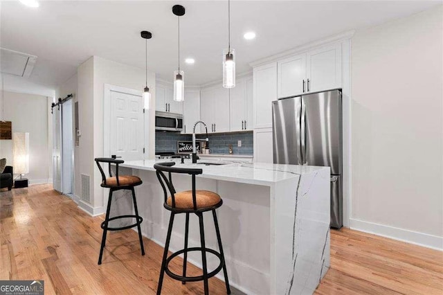 kitchen with white cabinetry, stainless steel appliances, an island with sink, a barn door, and light wood-type flooring