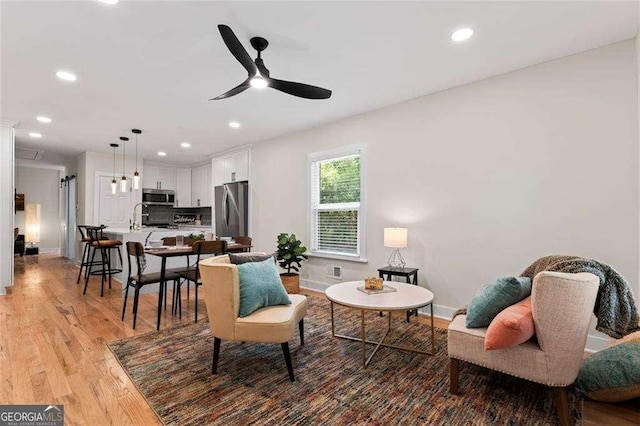 living room with sink, light hardwood / wood-style floors, and ceiling fan