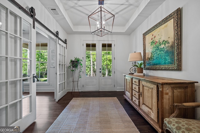 entryway with french doors, dark hardwood / wood-style flooring, a raised ceiling, a notable chandelier, and a barn door