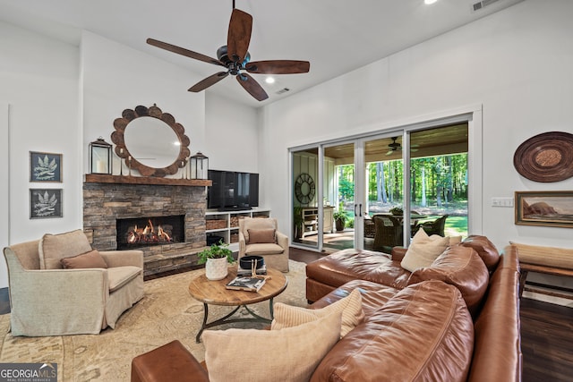 living room featuring ceiling fan, a stone fireplace, hardwood / wood-style floors, and a high ceiling