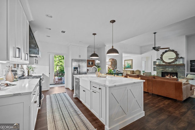 kitchen featuring appliances with stainless steel finishes, pendant lighting, light stone countertops, a kitchen island with sink, and white cabinets