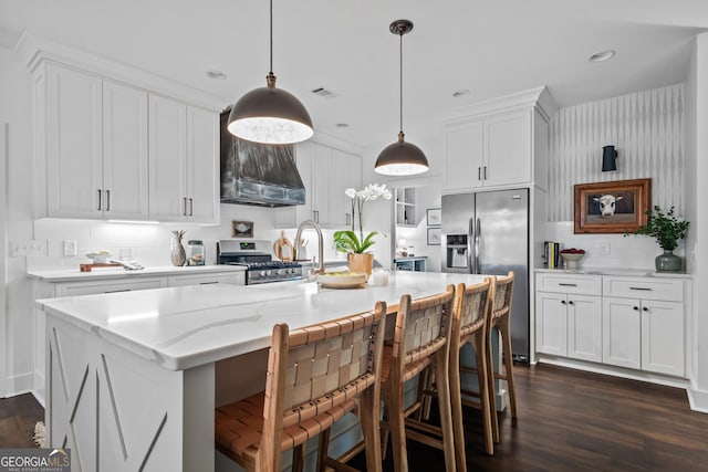 kitchen featuring a breakfast bar, decorative light fixtures, a center island with sink, appliances with stainless steel finishes, and white cabinets