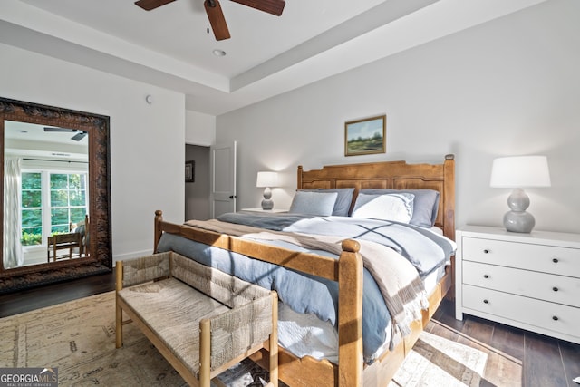 bedroom with ceiling fan, access to exterior, dark hardwood / wood-style flooring, and a tray ceiling