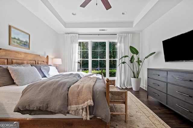 bedroom with a raised ceiling, dark wood-type flooring, and ceiling fan