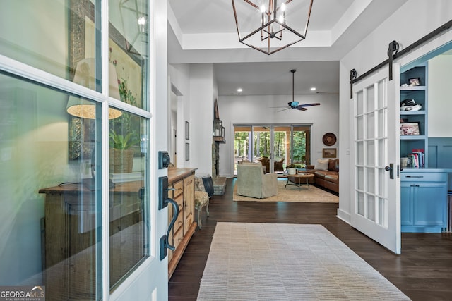 foyer with a barn door, dark hardwood / wood-style floors, ceiling fan, and a tray ceiling