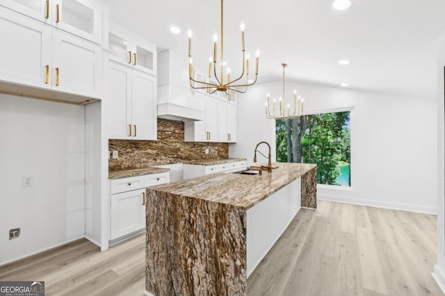 kitchen featuring white cabinetry, a kitchen island with sink, decorative light fixtures, light stone countertops, and sink