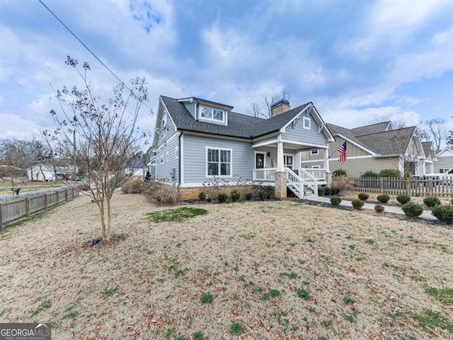 view of front of home with a shingled roof, a porch, a chimney, and fence