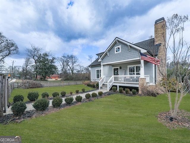 rear view of property with a yard, covered porch, a chimney, and fence