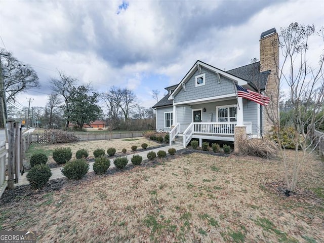 view of front of house with covered porch, a chimney, roof with shingles, and fence