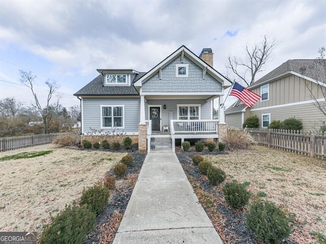 view of front of property with a shingled roof, a porch, a chimney, and fence