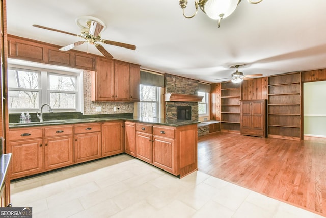 kitchen featuring a fireplace, kitchen peninsula, light wood-type flooring, sink, and ceiling fan