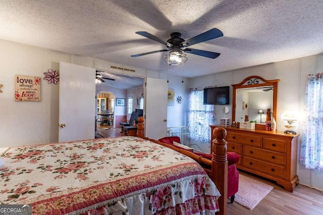 bedroom with ceiling fan, light hardwood / wood-style floors, and a textured ceiling