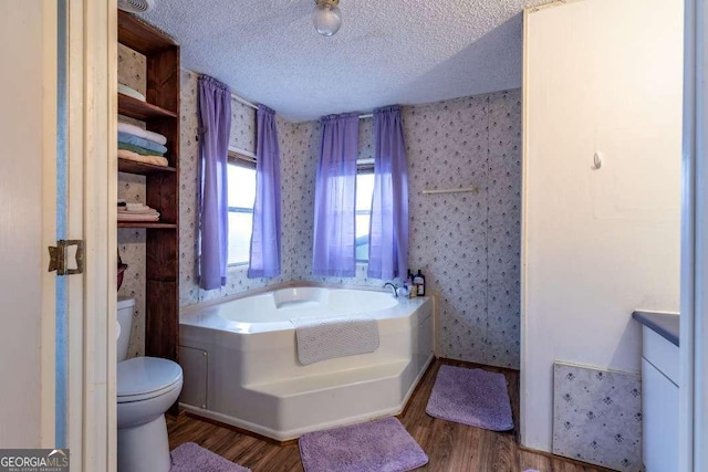 bathroom featuring hardwood / wood-style flooring, a tub to relax in, a textured ceiling, and toilet